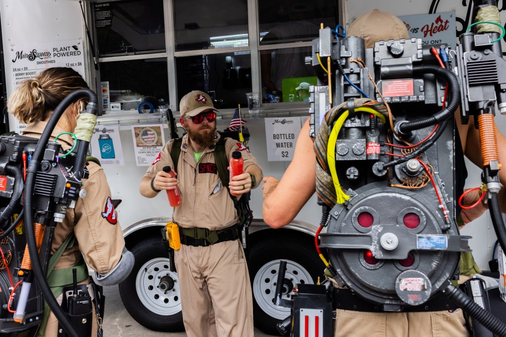 Yellow Rose Ghostbusters’ Alex Spence, 32, passes a refreshment to his fellow Ghostbuster Cory Micheletti, right, 43, at the 128th Annual Friendswood 4th of July Celebration