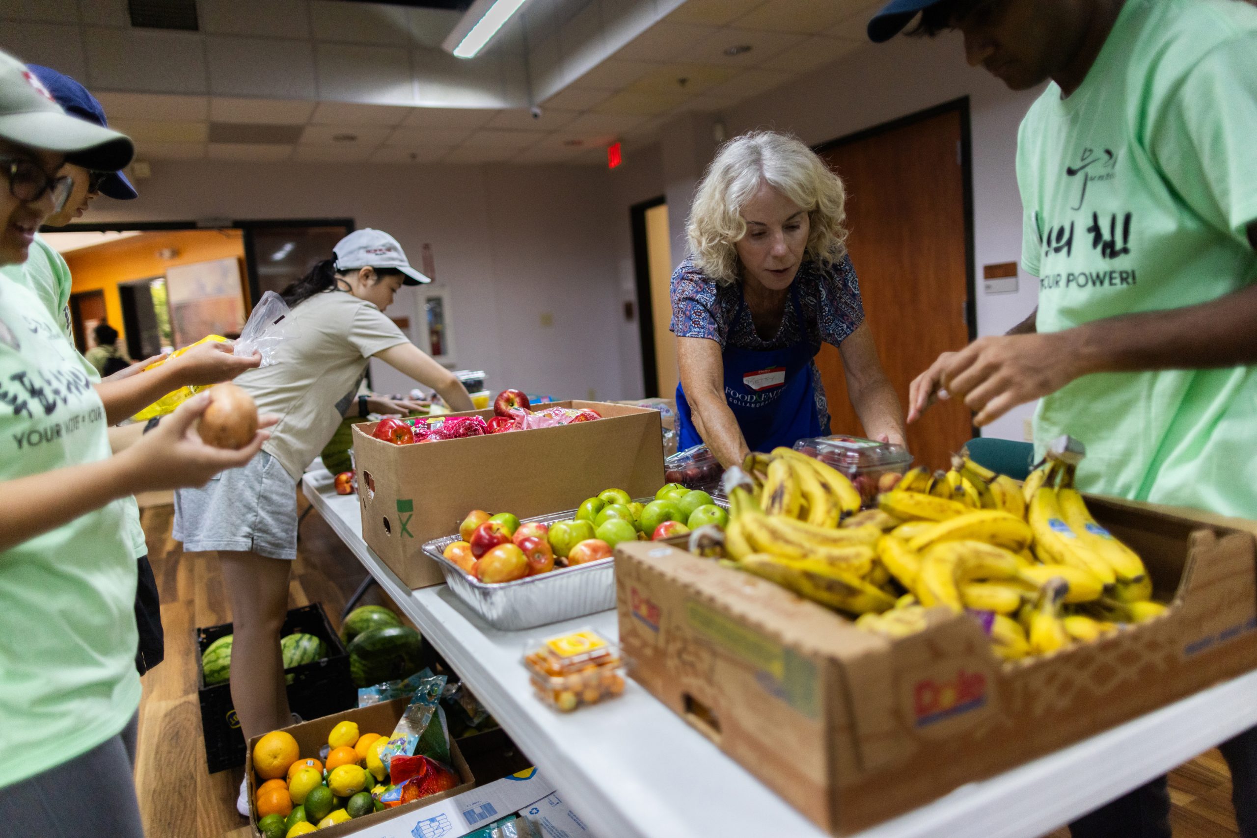 Volunteer Betsy Torrence, center, helps place fresh produce on a table to make the food presentable