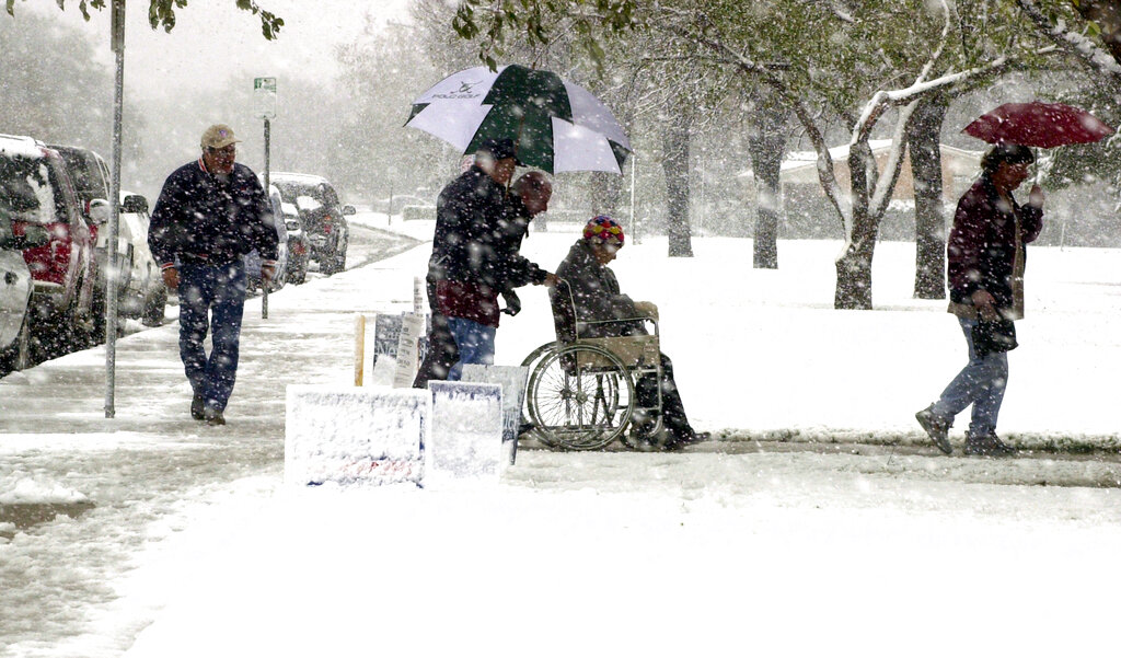 Ross Fewell, center with umbrella, and Randy Willis escort Janice Fewell in a wheelchair through the snow as they and other voters prepare to cast their ballots in Precinct 28, at Parsons Elementary School, in Lubbock, Texas