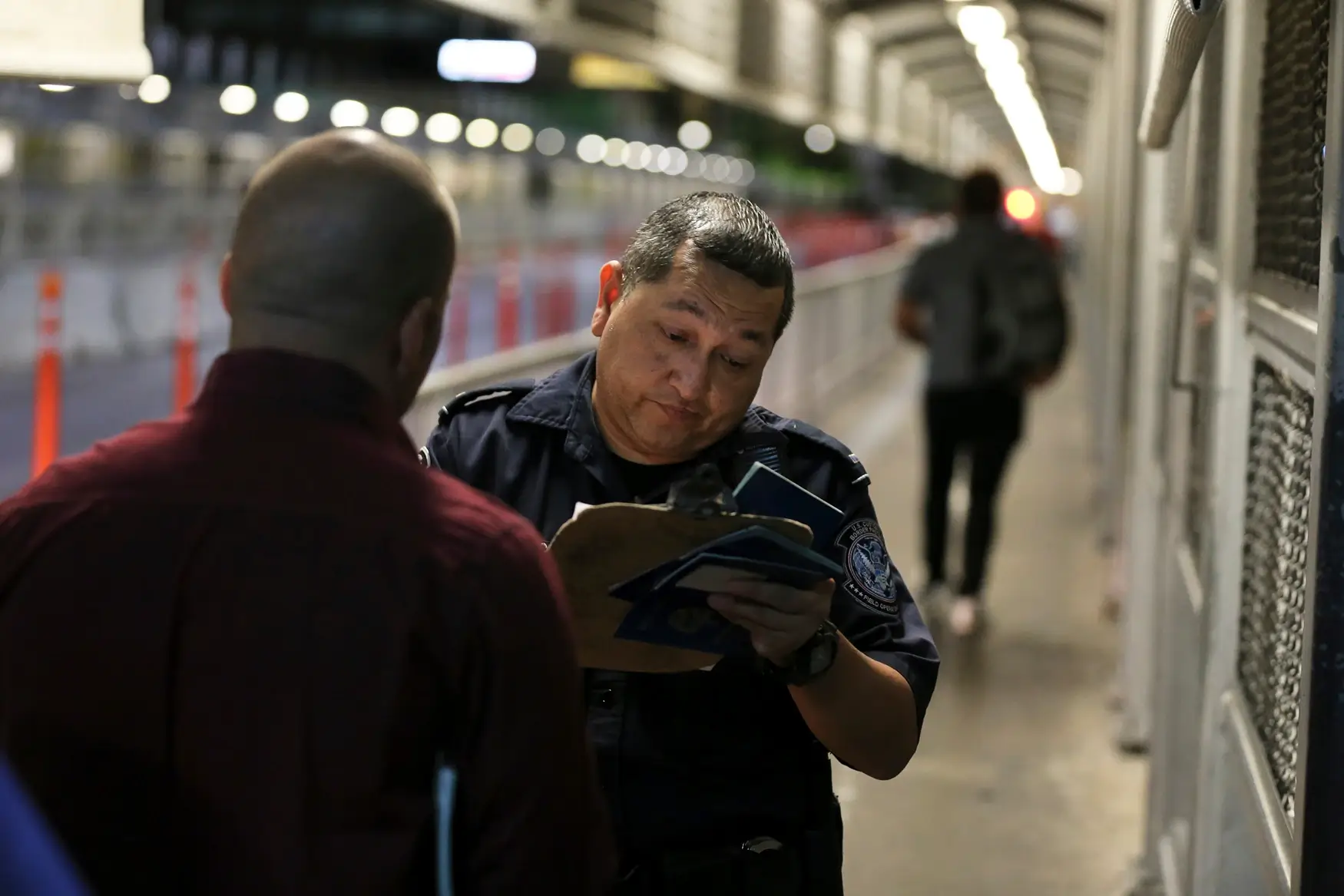 A U.S. Customs and Border Protection officer checks the documents of migrants who are on their way to apply for asylum in the United States, on International Bridge 1 as they depart Nuevo Laredo, Mexico, early Tuesday, Sept. 17, 2019. Tent courtrooms opened Monday in two Texas border cities to help process thousands of migrants who are being forced to wait in Mexico while their requests for asylum wind through clogged immigration courts.