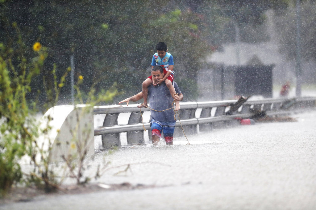A man wades through floodwaters with a child on his shoulders after the remnants of Hurricane Harvey struck Houston
